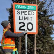 Worker installs a Vision Zero street sign.
