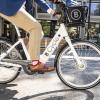 Image of person riding white ebike on street adjacent to shopping center.