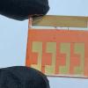 Fingers holding a small materials solar test device