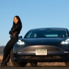 Kyri Baker stood next to a Tesla with a wind turbine in the background