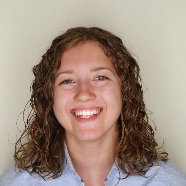 Portrait of Katie smiling with curly hair and a button down shirt.