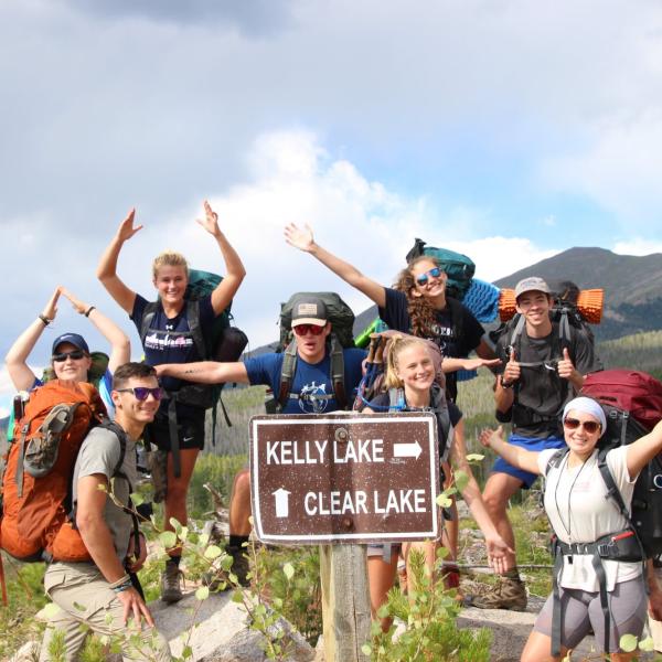 incoming students posing by a sign with backpacks on