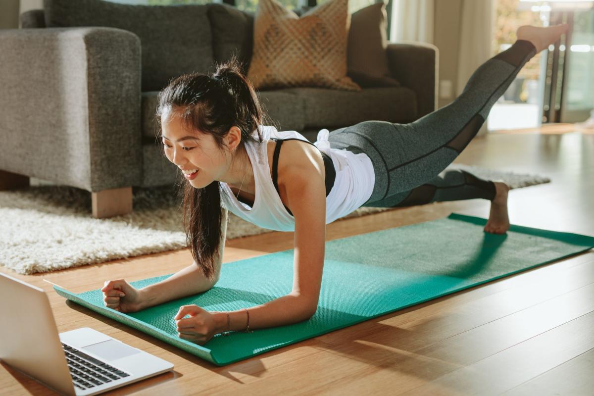woman on yoga mat watching laptop