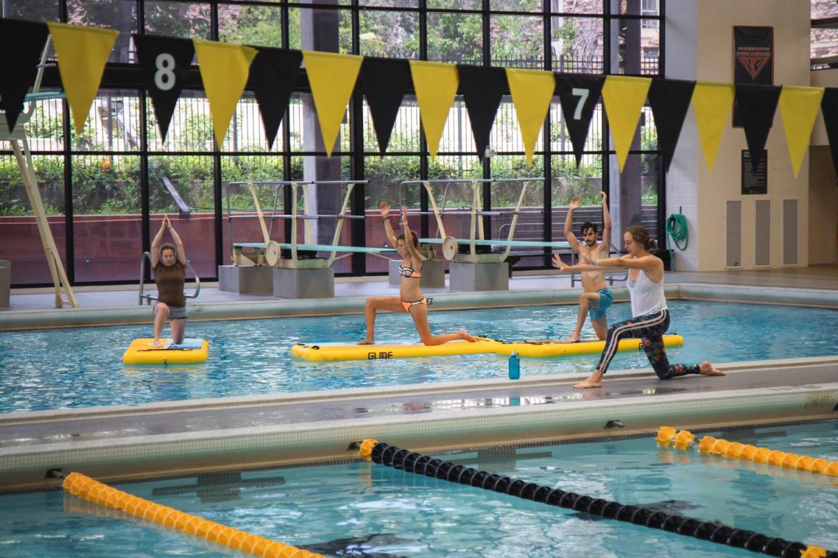 instructor guiding students in paddleboard yoga class at indoor pool
