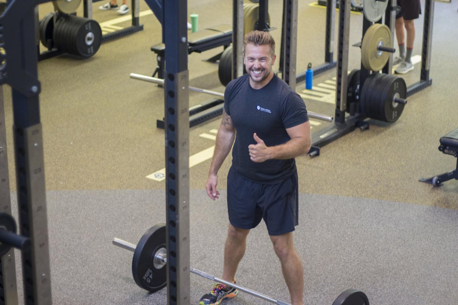 Personal Trainer giving a thumbs up next to barbells in the weight room
