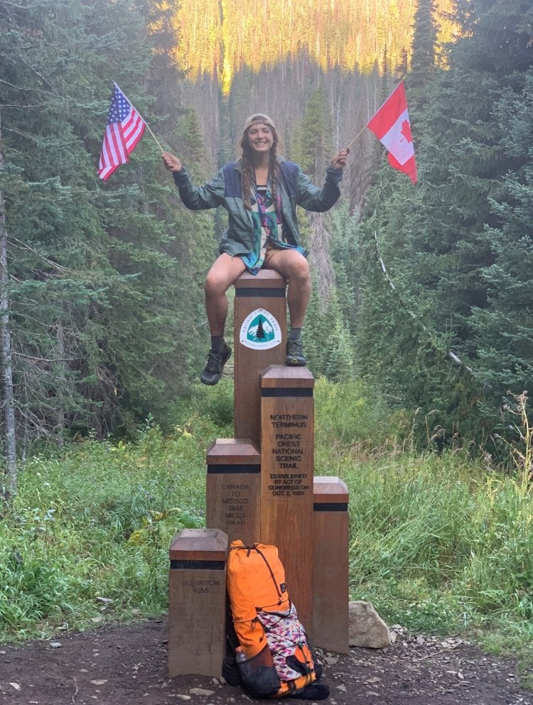 woman sitting on a mile marker holding up an american and canadian flag