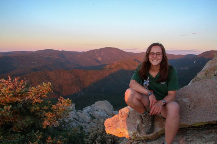 woman sitting on cliffs edge overlooking a mountain range