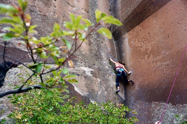 Ella climbing up the corner of a cliff