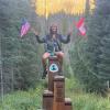 woman sitting on a mile marker holding up an american and canadian flag