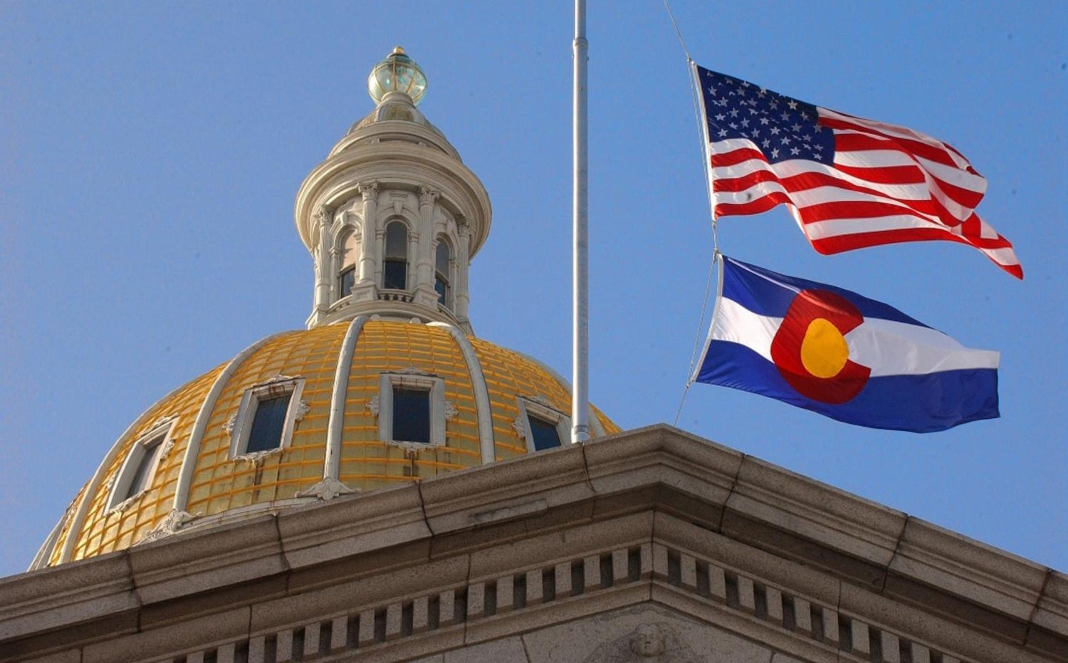 A view of the U.S. and Colorado state flags flying over the Colorado State Capitol Building.