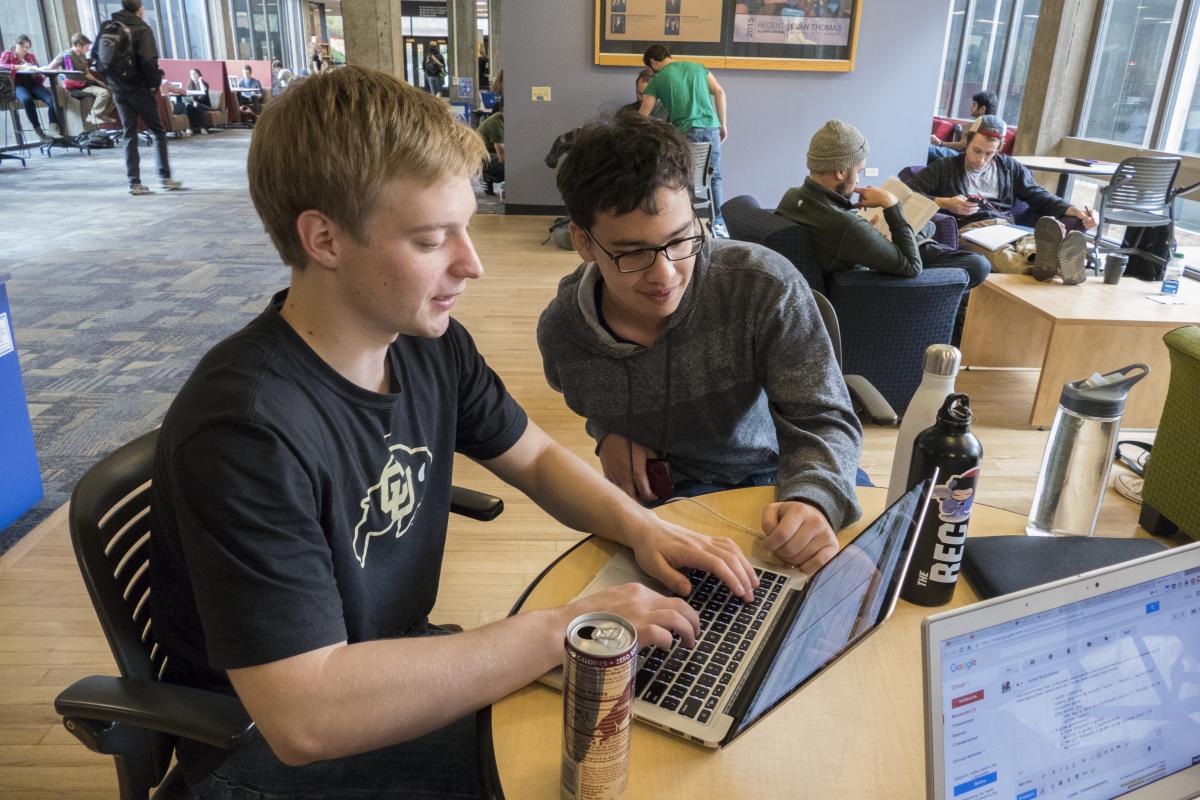 Two students work together on a laptop in a shared space.