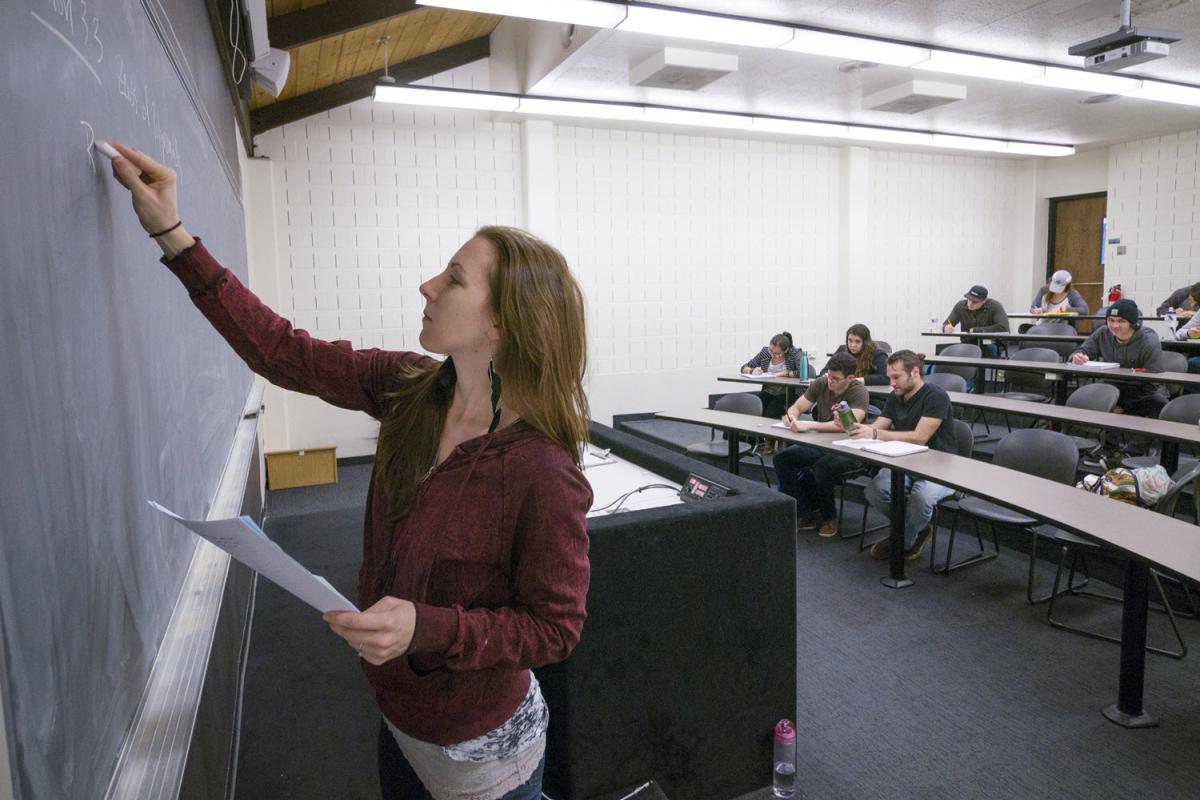 An instructor writes on a chalkboard.