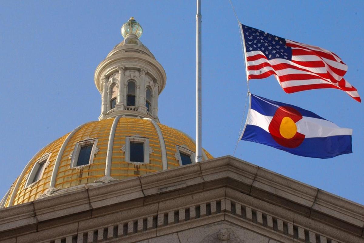 A view of the U.S. and Colorado state flags flying over the Colorado State Capitol Building.