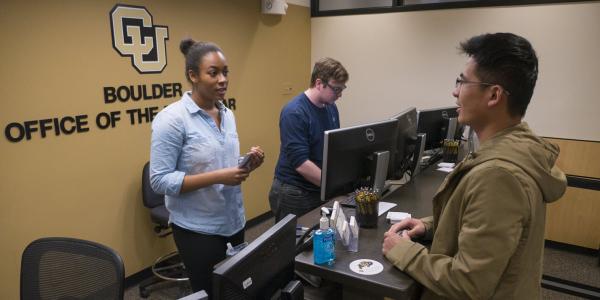 Two Office of the Registrar student employees help a student at the reception desk