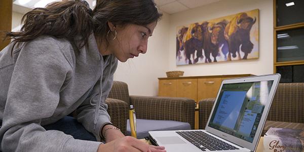 A student writes notes while consulting her laptop in the Office of the Registrar lobby.