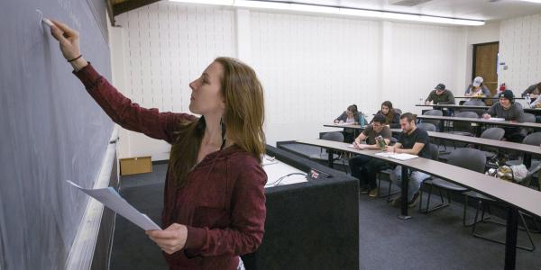 An instructor writes on a chalkboard.