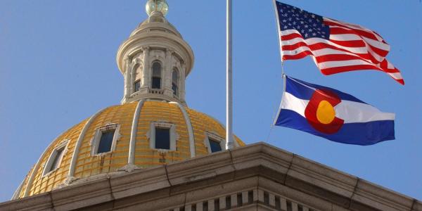 A view of the U.S. and Colorado state flags flying over the Colorado State Capitol Building.