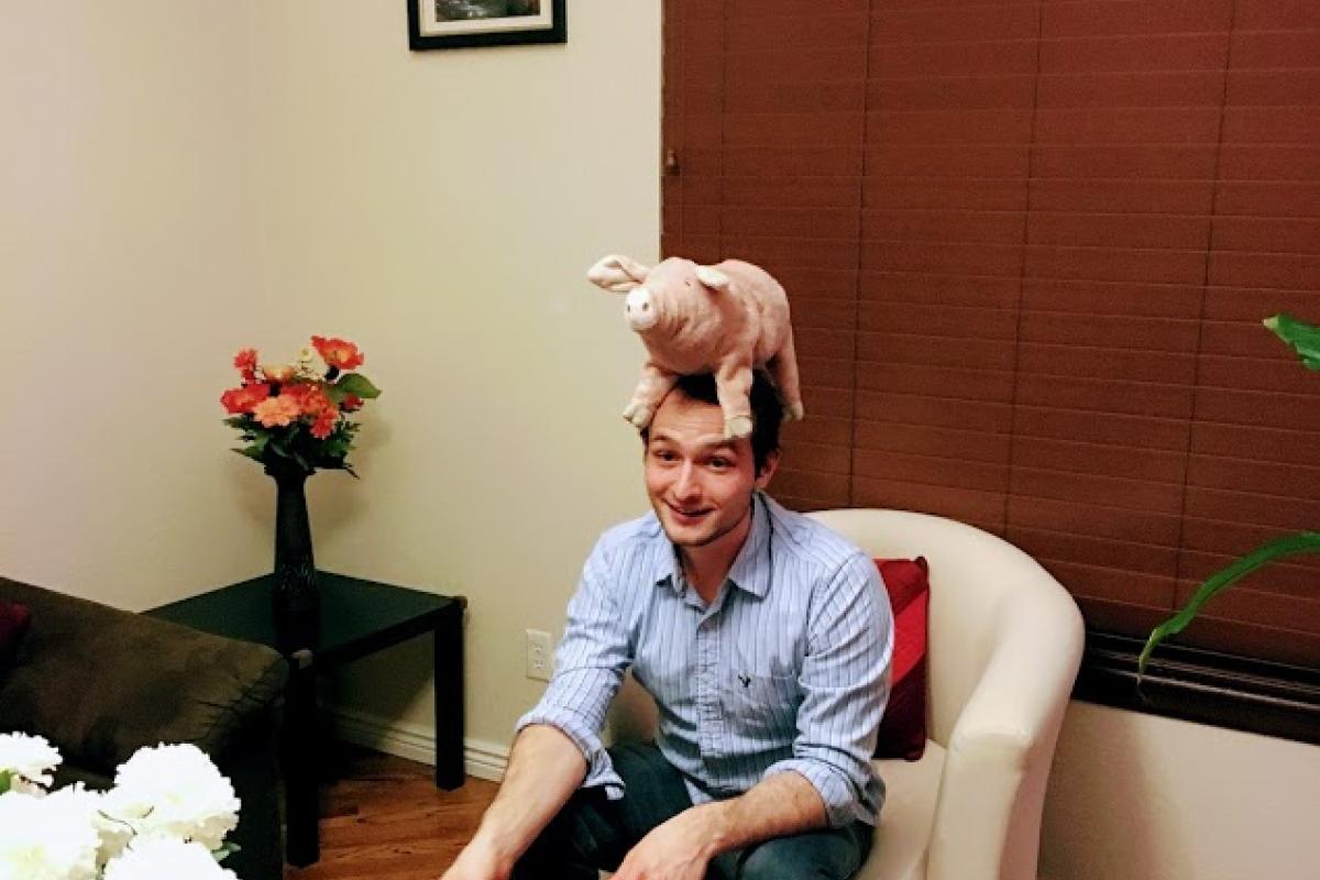 A man sitting down with a pig doll on his head
