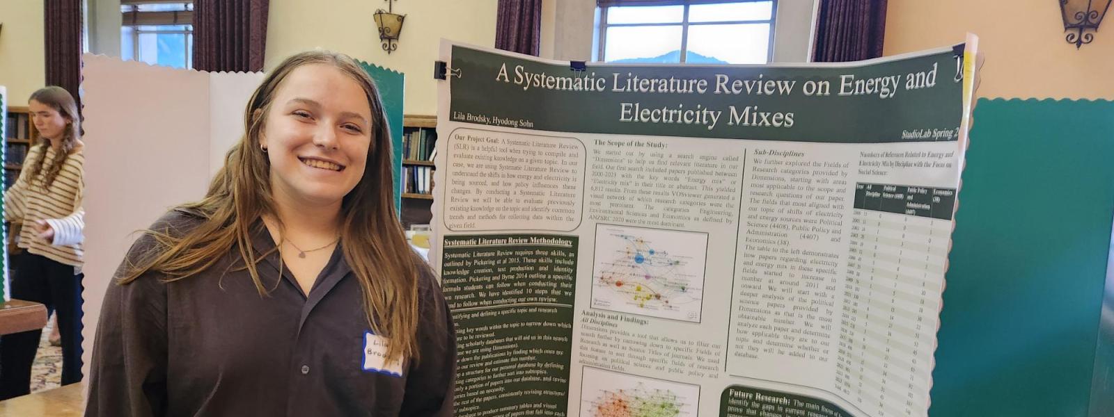 Student poses and smiles next to her poster.
