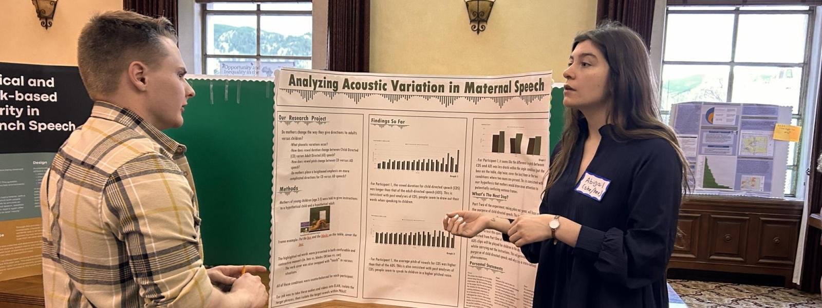 A student discusses her poster with another individual.