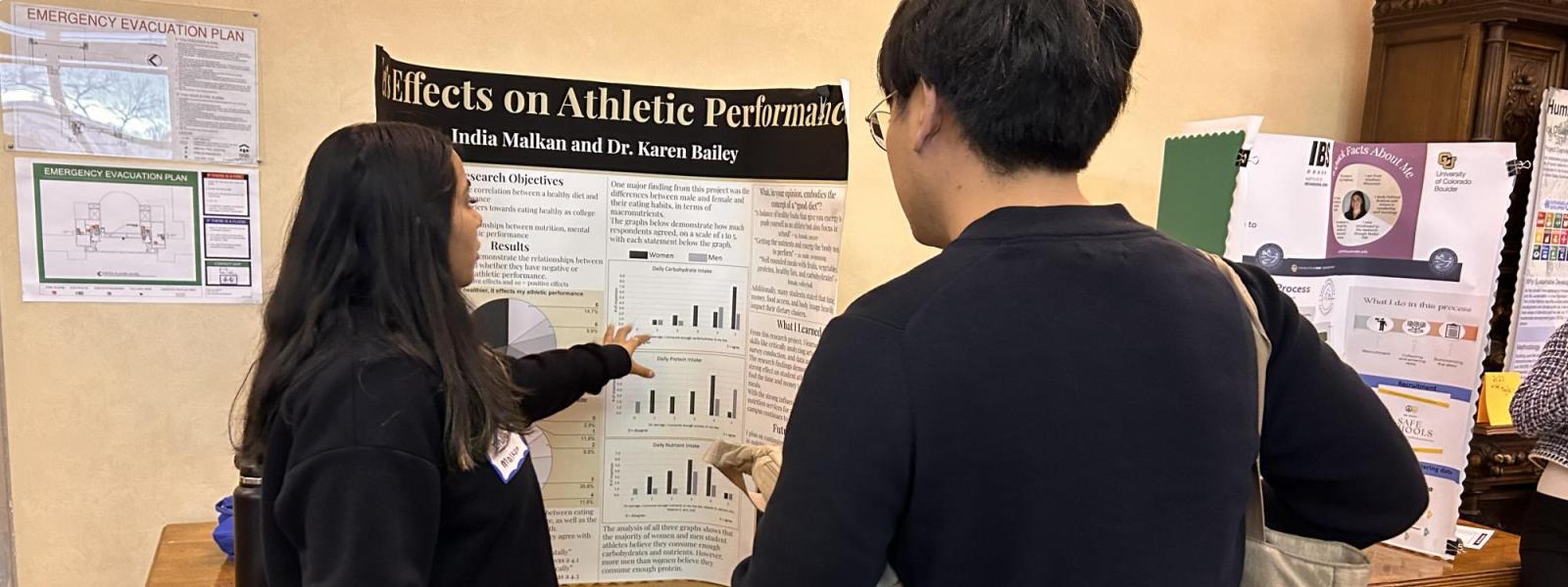 A student explains her poster to an individual.