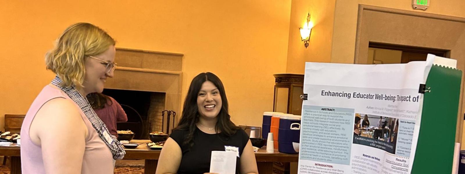 A student and professor smile next to a poster.