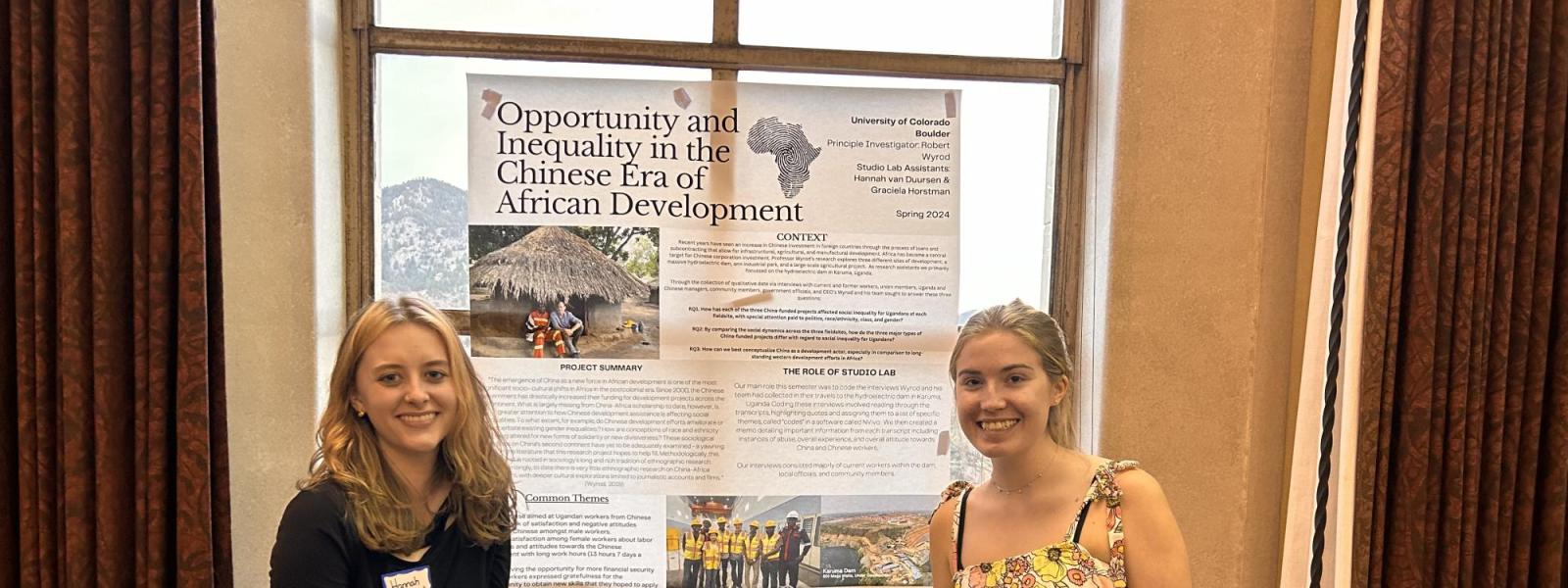 Two students pose with a poster centered.