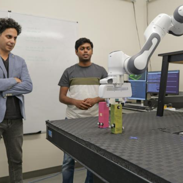 Graduate student Karan Muvvala watches as a robotic arm completes a task using wooden blocks