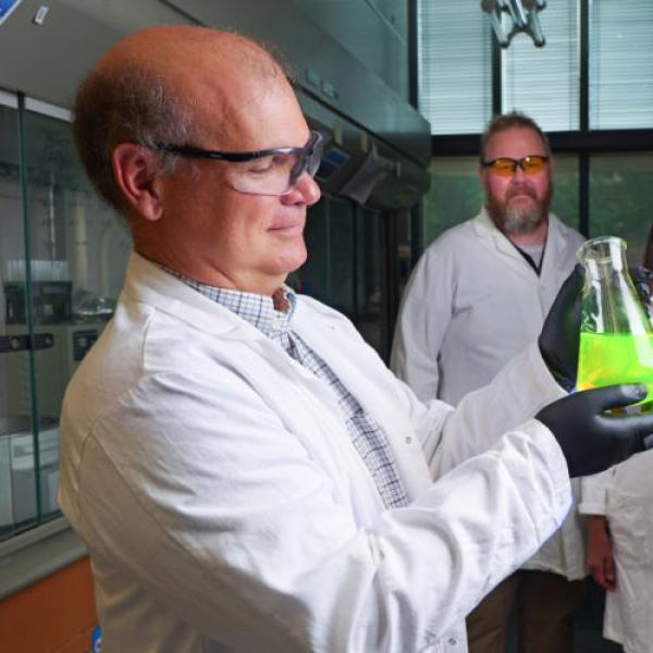 Christopher Bowman holds a beaker of hydrogel while his graduate student illuminates it with a flashlight