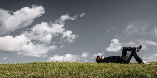 Man lying on the grass looking up at wide sky with clouds.