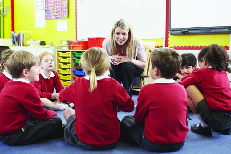 Female teacher with group of young students sitting in a circle.