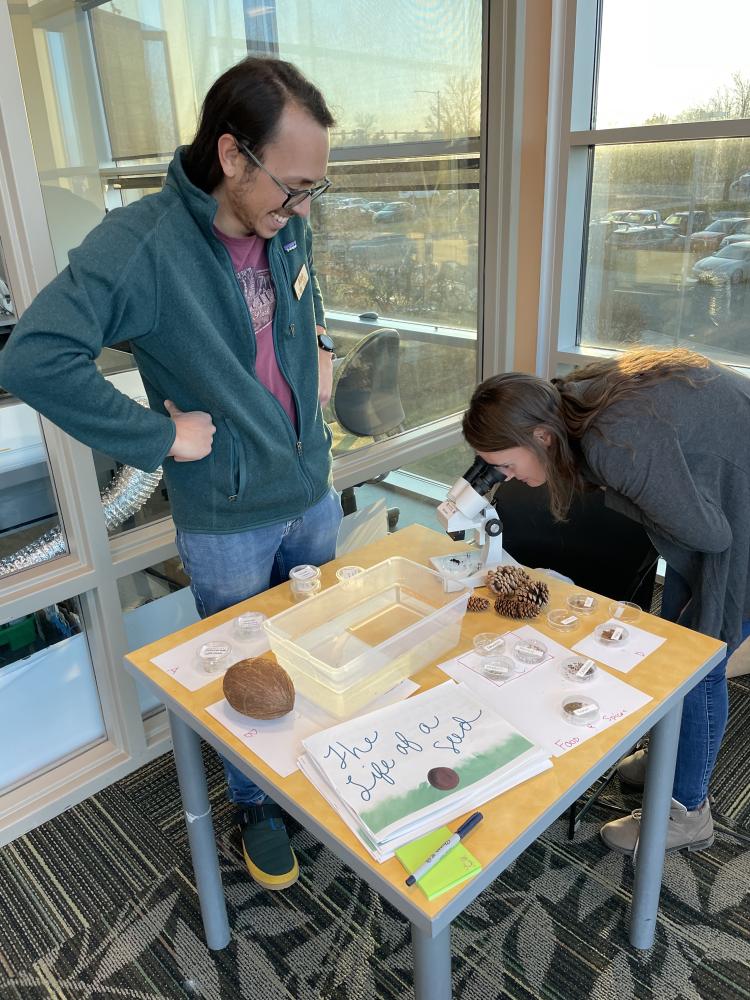 attendee looking through microscope as scientist looks on