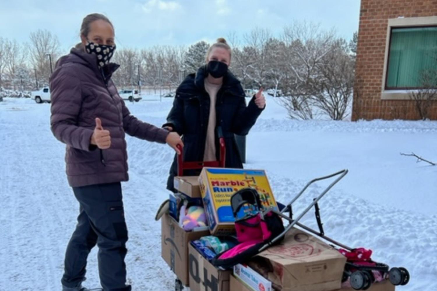 2 staff members in the snow with a dolly full of donations