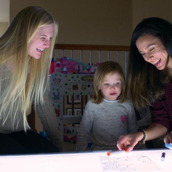Researcher and children smiling at light table