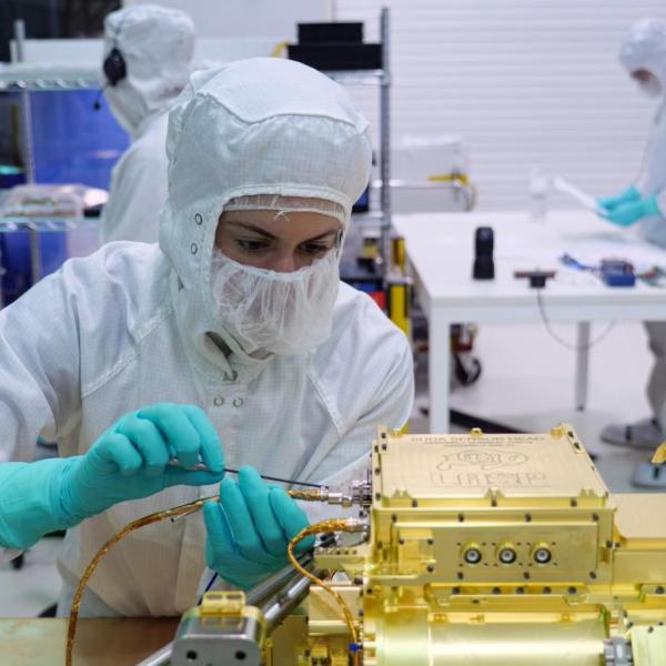 An engineer makes an electrical connection to the sensor head for Europa Clipper’s dust analyzer.