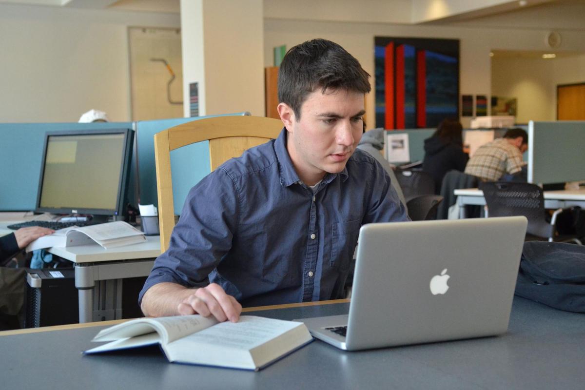 Student looking at laptop and book