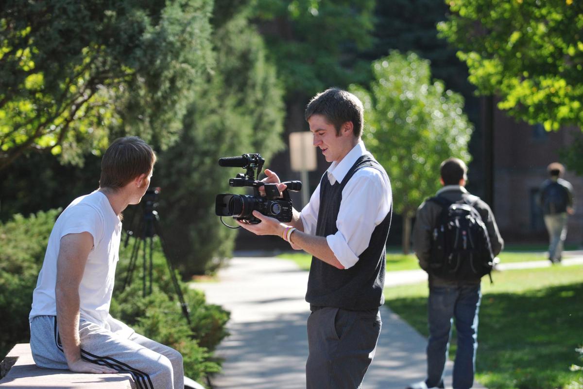 Student with video camera filming another student on campus