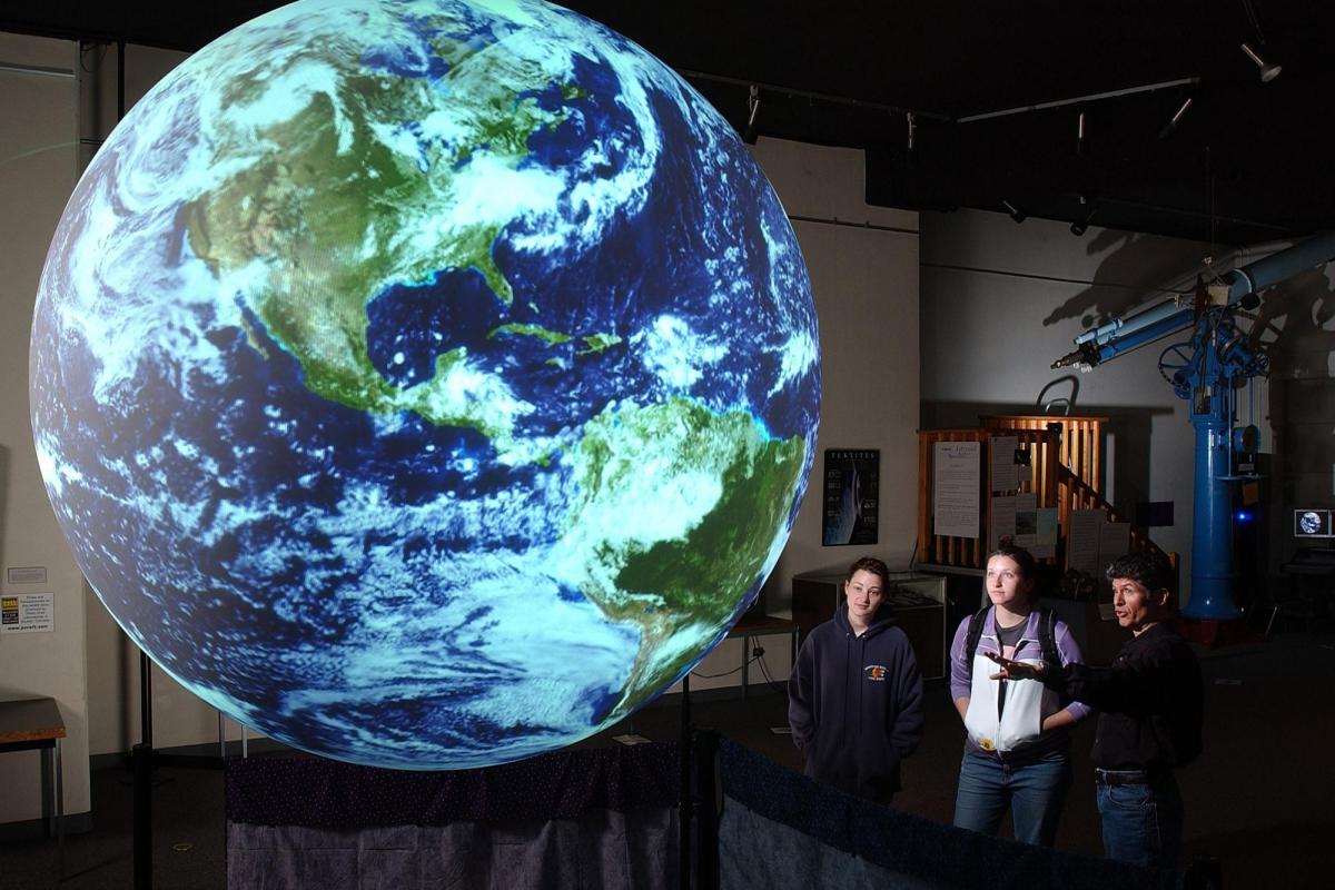 Students looking at lighted globe or Earth