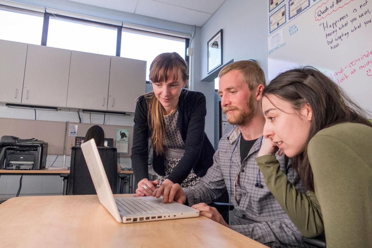 Students and faculty looking at laptop