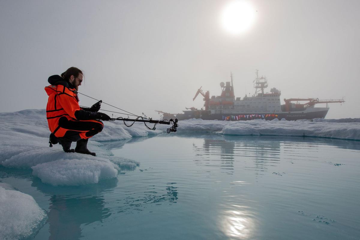 Scientist in the arctic with ship in the background