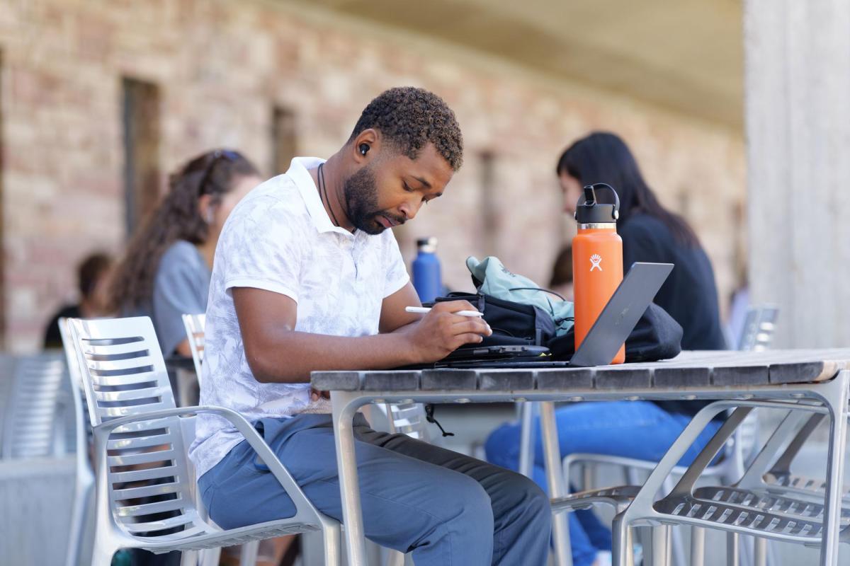Student sitting at patio table looking at laptop