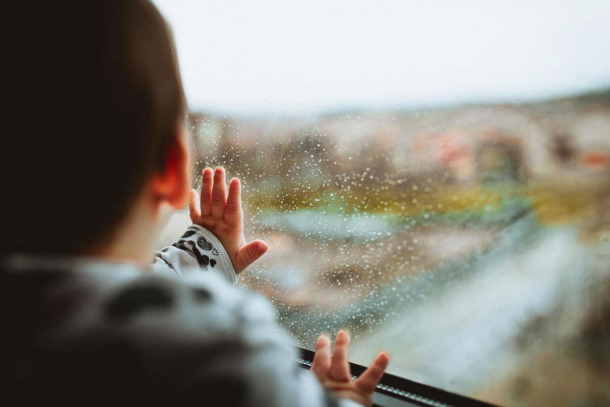 Toddler pushing hand against rainy window and looking outside