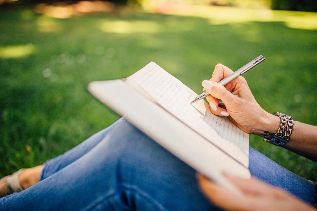 Person writing in notebook while sitting outside on lawn