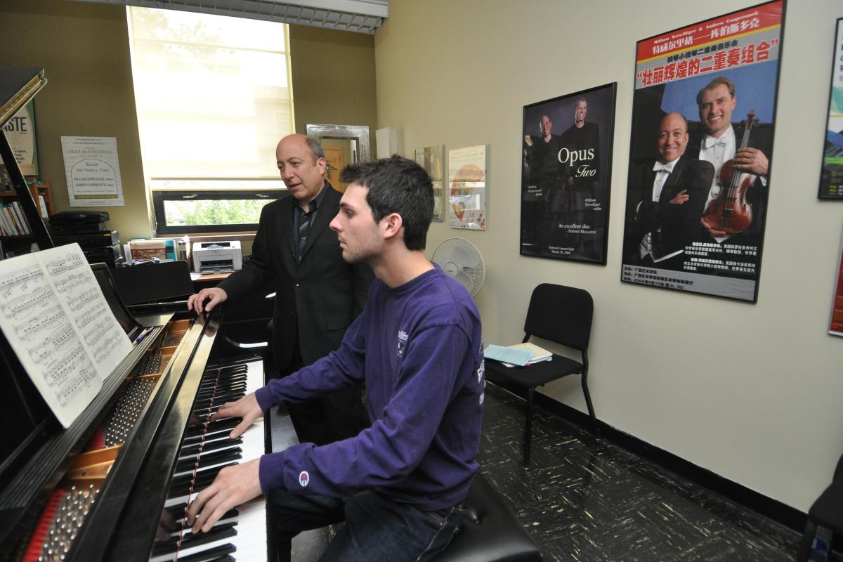 Student playing the piano with his instructor looking on