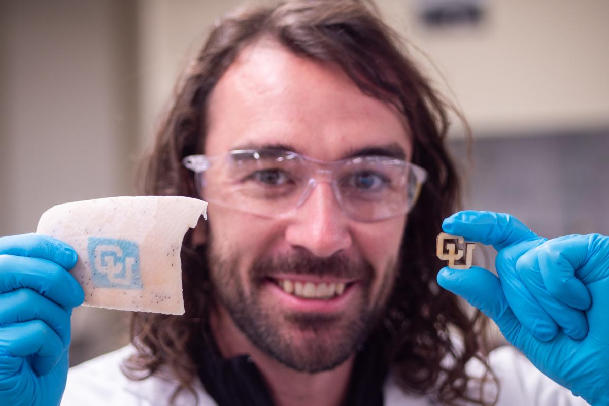 Assistant professor holds up the CU logo