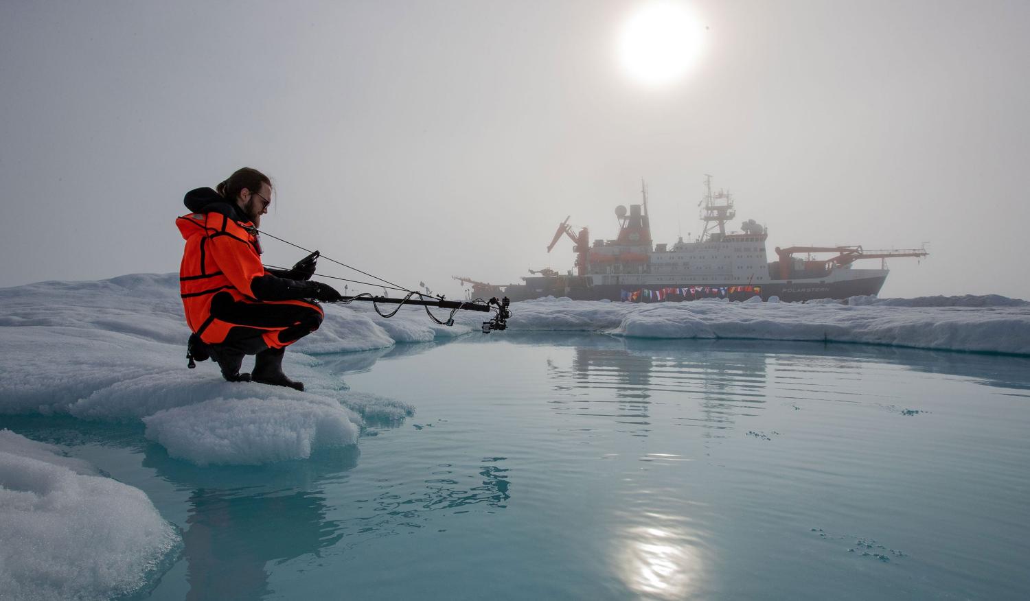 Scientist in the arctic with ship in the background