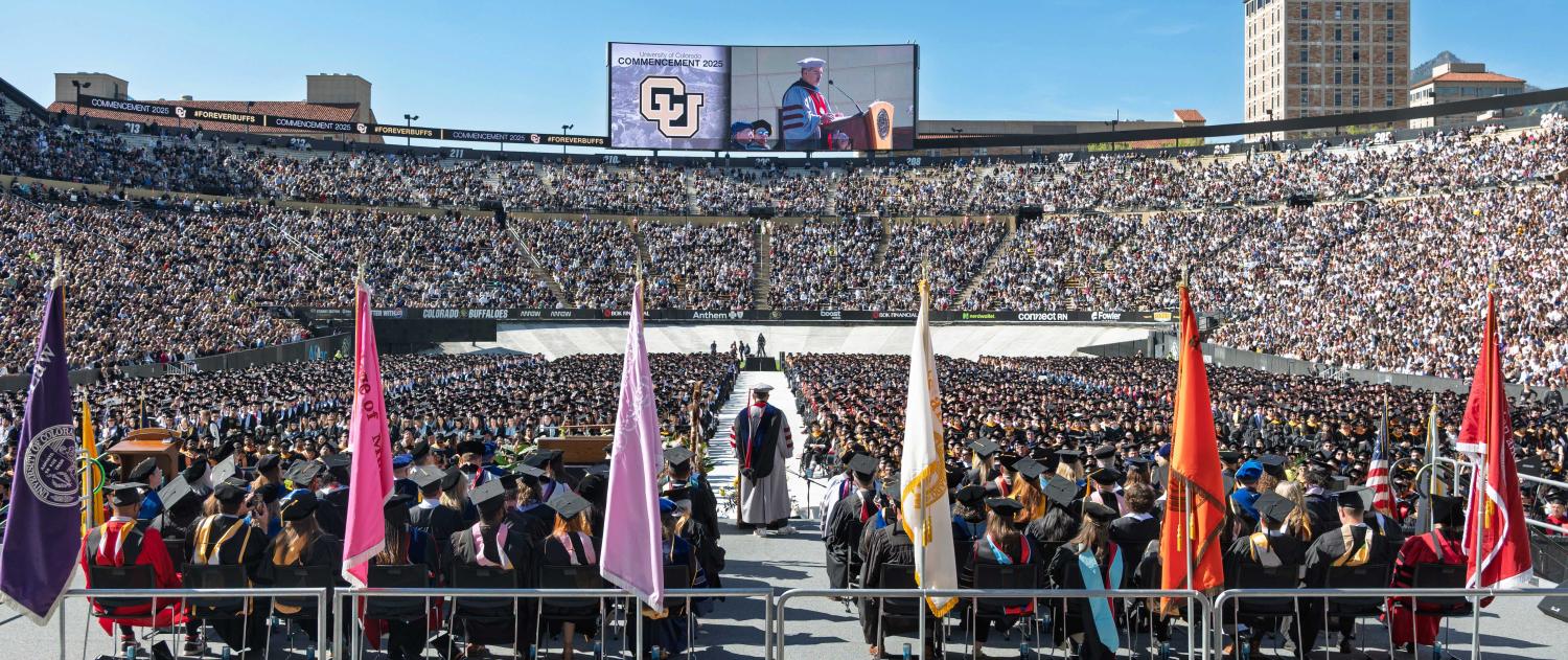 CU Boulder Commencement at Folsom Field. The field is filled with graduating students and the stands are filled with friends and family.