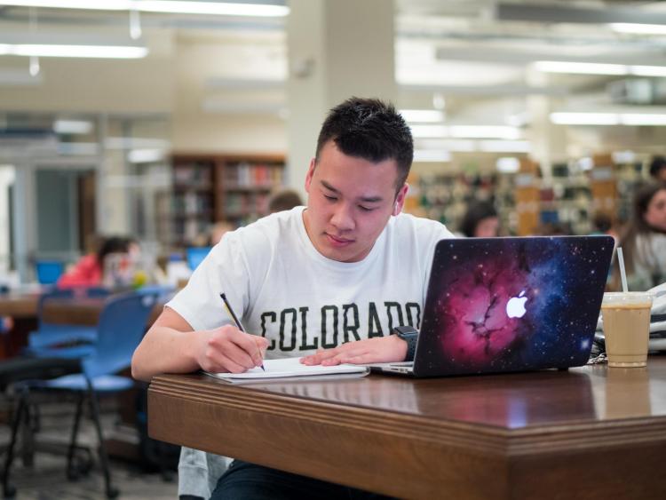 Student sitting at desk in library and writing
