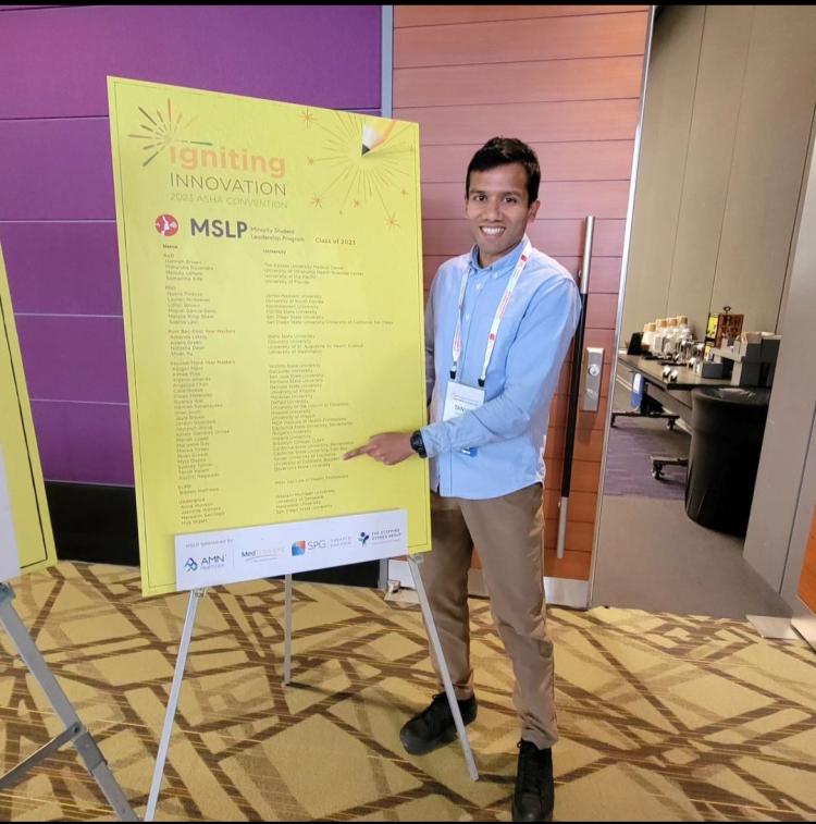 2nd Year MASLP student Tanvir Kalam in front of ASHA Poster
