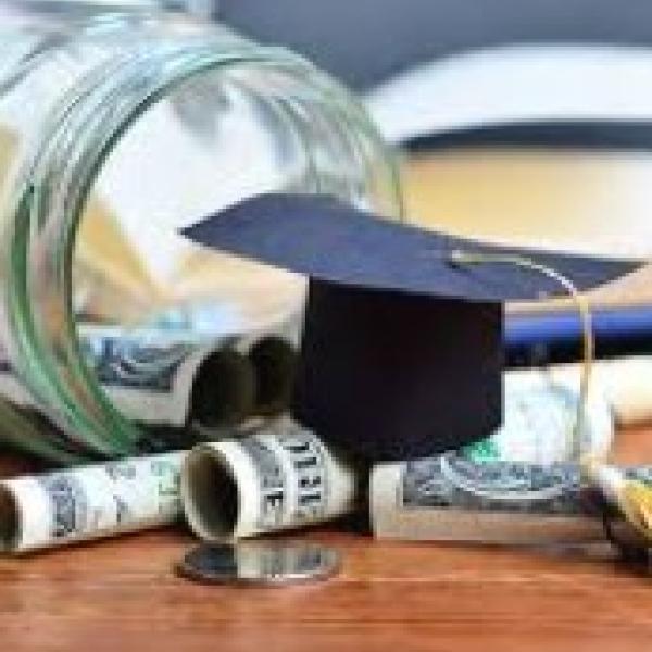 Glass jar spilling out with money and graduation cap